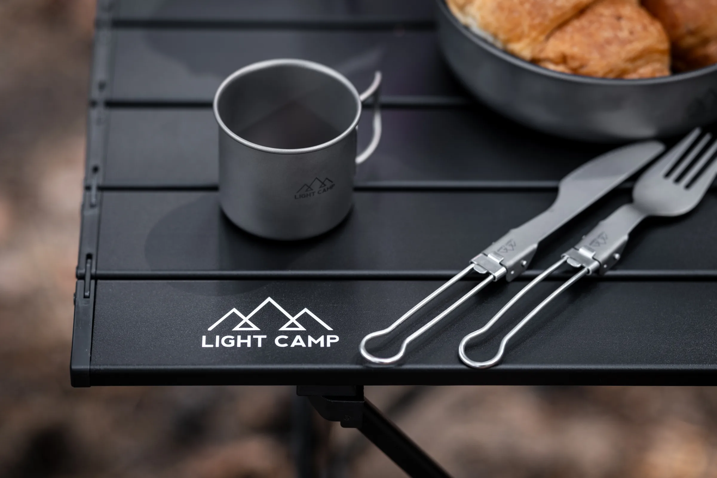 Чёрный столик для кемпинга Light Camp с металлической кружкой, столовыми приборами и миской с печеньем, предметная съёмка